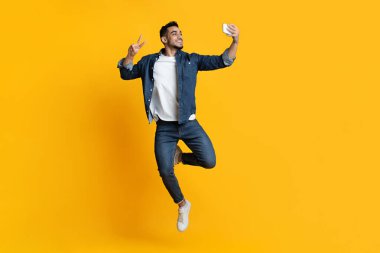 Neşeli yakışıklı Arap adam sarıda selfie çekiyor.