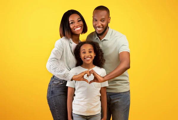 Feliz família amorosa. Preto pais de mãos dadas em forma de coração sinal, posando com a filha liitle sobre fundo amarelo — Fotografia de Stock