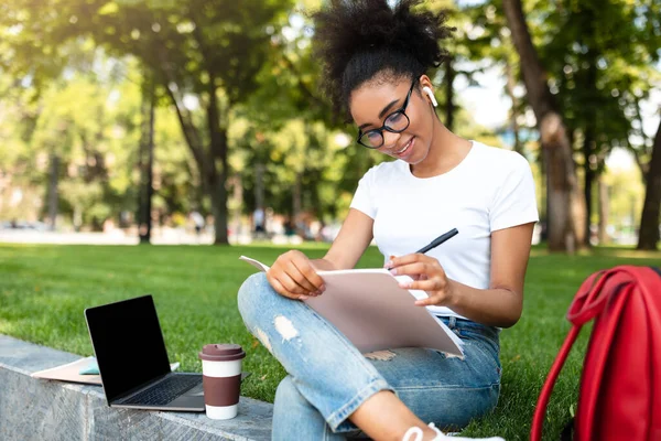 Preto estudante menina tomando notas aprendendo com laptop no parque — Fotografia de Stock