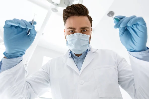 Muž zubař v masce obličeje a rukavice drží zubní nástroje — Stock fotografie