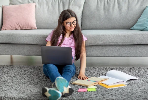 Chica adolescente india enfocada sentada en el piso con computadora portátil y materiales de estudio, aprendiendo en línea desde casa, espacio libre — Foto de Stock