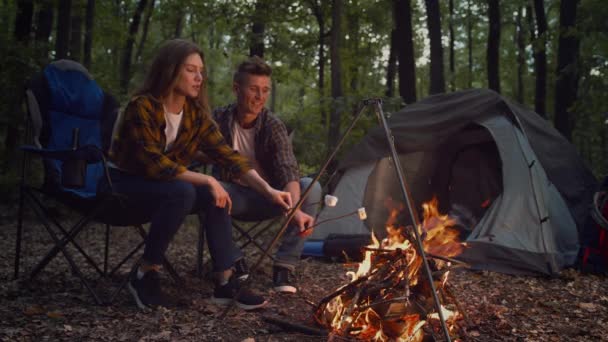 Romantický koncept víkendu. Mladý pár zamilovaný smažení marshmallow v ohni, tráví aktivní volný čas v lese — Stock video
