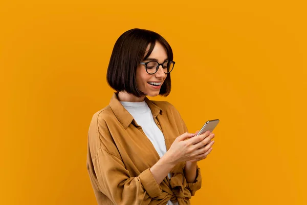 现代通信。千禧年女士在智能手机上浏览，在网上与朋友聊天，黄色背景 — 图库照片