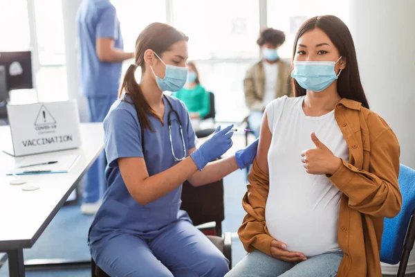 Těhotná žena v masce dostávající koronavirovou vakcínu ukazující palce nahoru — Stock fotografie
