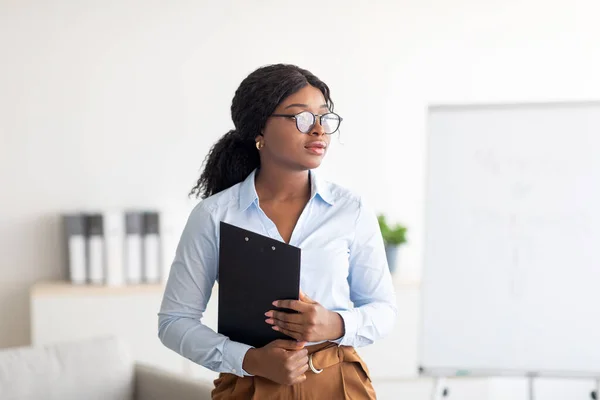 Porträtt av fokuserad svart kvinnlig psykoterapeut med Urklipp tittar åt sidan djupt i tanken på moderna kontor — Stockfoto