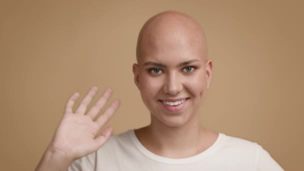 Mulher jovem sem cabelo acenando mão sorrindo posando no fundo bege — Vídeo de Stock