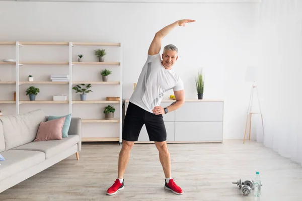 Aktif yaşam tarzı. Daha sağlıklı bir yaşam için esneklik egzersizleri yapan olgun bir adam, evde egzersiz yapan, boş bir alan. — Stok fotoğraf