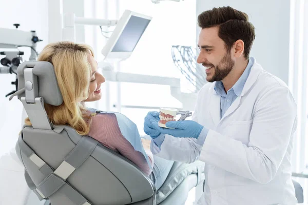 Neşeli doktor dişçi hastaya çene minyatürünü gösteriyor — Stok fotoğraf