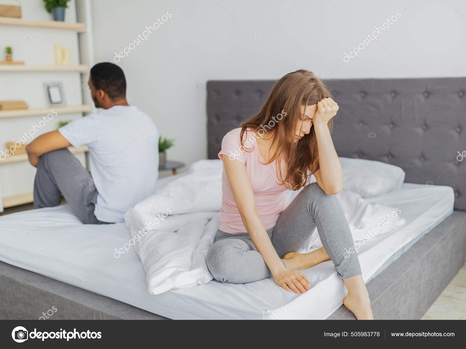 Young interracial couple having relationship difficulties, sitting on opposite sides of bed, not looking at each other Stock Photo by ©Milkos 505983778