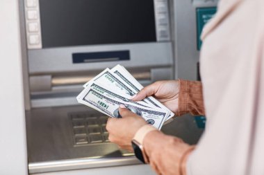 Tanınmayan Arap kadın para çekiyor, ATM yakınlarında dolar sayıyor.