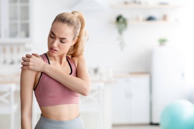 Evdeki antrenmandan sonra omuz ağrısı çeken üzgün, beyaz, sarışın bir bayan.