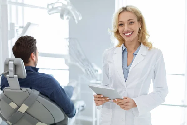 Mujer alegre dentista con tableta digital sonriendo a la cámara —  Fotos de Stock