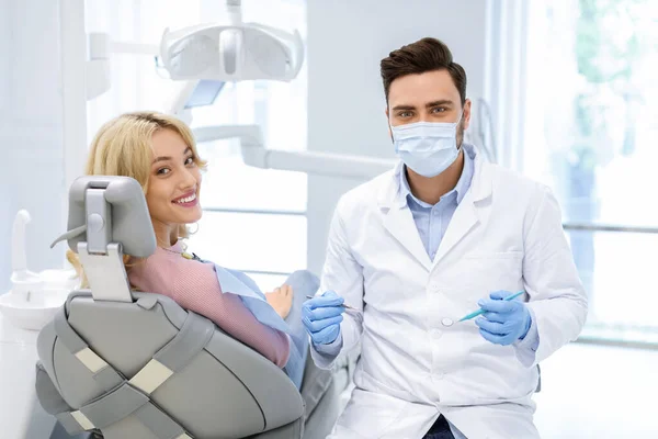 Potilas ja mies lääkäri hammaslääkärin työkalut katsot kameraa — kuvapankkivalokuva