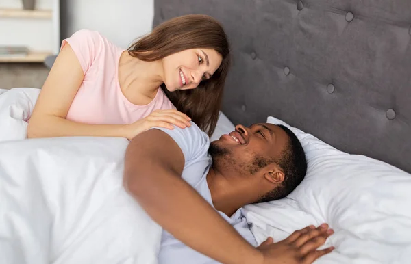 Люблячи одружену різноманітну пару розслабляючись, дивлячись один на одного в ліжку вдома, відчуваючи себе безтурботним і щасливим вранці — стокове фото