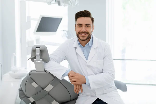 Dentista atraente sorrindo para a câmera, posando no armário dentário — Fotografia de Stock