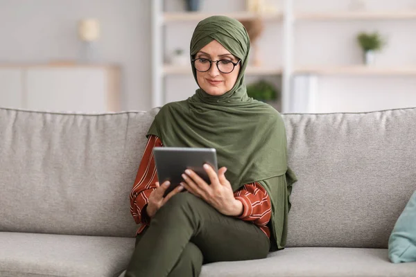 Senior musulmana mujer usando tableta digital lectura libro en línea interior — Foto de Stock