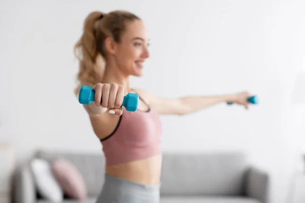 Cheerful european millennial blonde female lifting dumbbells at home, selective focus — Stock Photo, Image