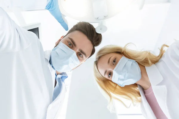 Dois dentistas em máscaras faciais e luvas de borracha, tiro de baixo ângulo — Fotografia de Stock
