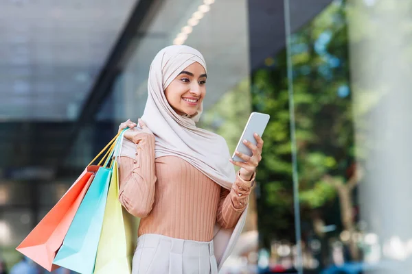 Tatmin olmuş genç orta doğulu, tesettürlü bir kadın, alışveriş merkezinin yakınındaki akıllı telefondan mesaj atıyor. — Stok fotoğraf