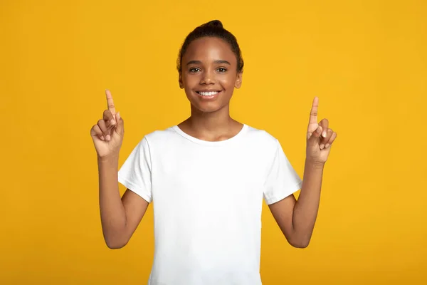 Senyum remaja african american gadis murid dalam t-shirt putih menunjuk jari sampai dengan ruang kosong — Stok Foto