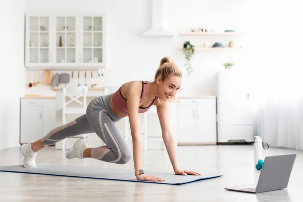 Leende kaukasier söt ung fitness kvinna gör ben övningar och titta på online-träning på laptop hemma — Stockfoto