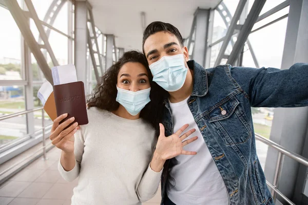 Viajes pandémicos. Emocionada pareja árabe en máscaras médicas tomando selfie en aeropuerto —  Fotos de Stock