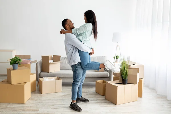 Любящая африканская американская пара празднует день переезда, парень поднимает свою жену в их новой квартире — стоковое фото