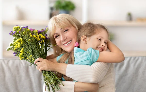 Feliz niño pequeño saludo feliz anciana con flores —  Fotos de Stock