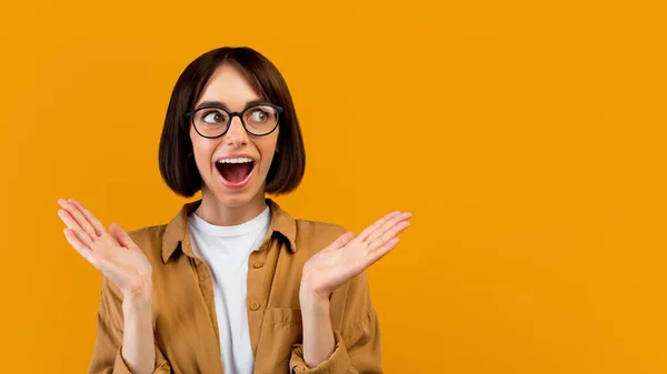 Giovane donna che esprime eccitazione, guardando da parte e bocca aperta a sorpresa, sfondo giallo con spazio libero — Foto Stock