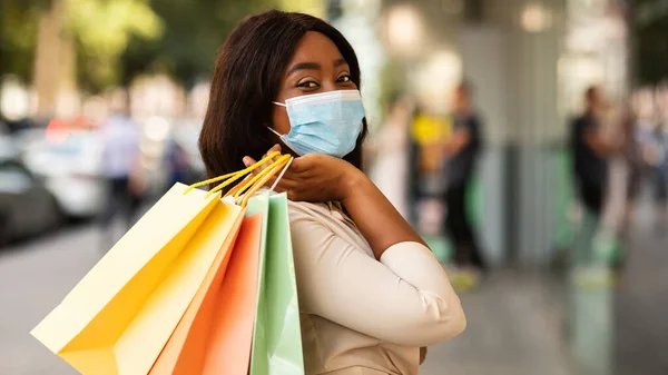 Zwarte vrouw in masker met boodschappentassen op zoek naar camera — Stockfoto