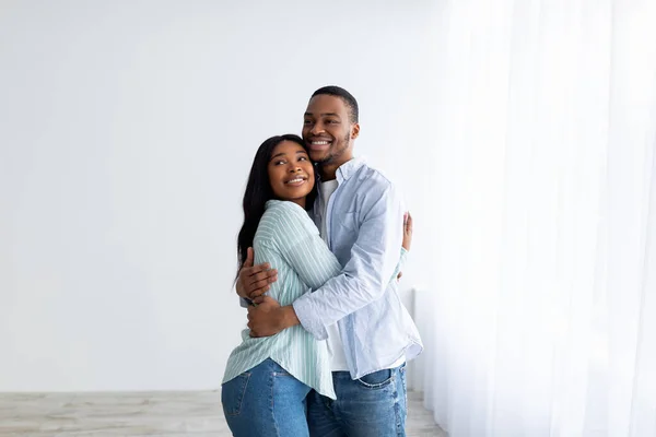 Happy young black spouses standing in their own house, hugging and smiling, being happy of buying own lodging — Stock Photo, Image