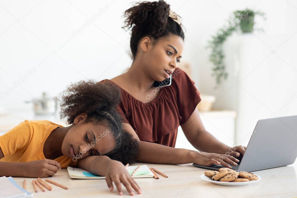 Bored teen girl sitting by her working mom, kitchen interior