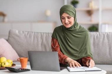 Üst düzey İslami İşkadını evde çalışan dizüstü bilgisayara not alıyor