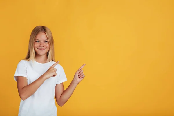 Sorrindo adolescente bonita loira menina pupila em branco t-shirt apontando os dedos para o espaço vazio — Fotografia de Stock