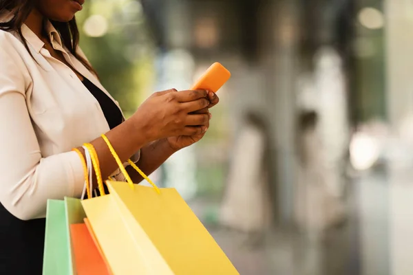 Glad svart kvinna med smartphone, hålla shoppingväskor — Stockfoto