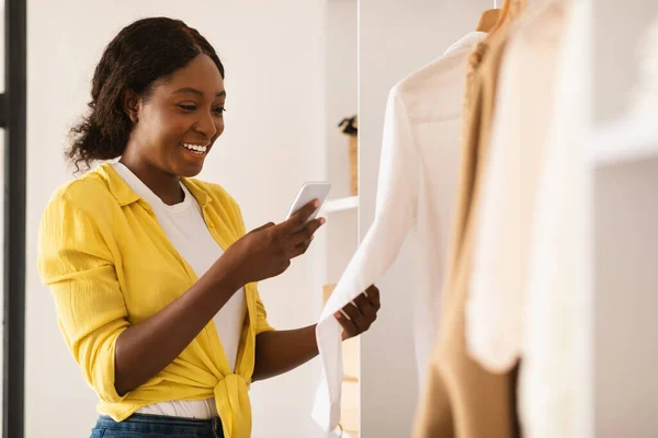 Senhora preta feliz usando Smartphone compra de roupas novas on-line no interior — Fotografia de Stock