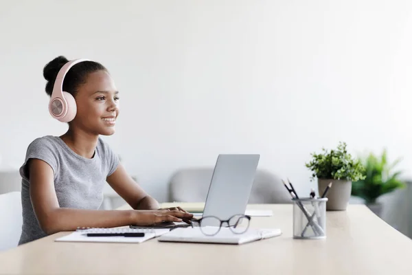 Glad tonåring afro amerikansk flicka i hörlurar titta på video lektion på distans på laptop i vardagsrummet interiör — Stockfoto