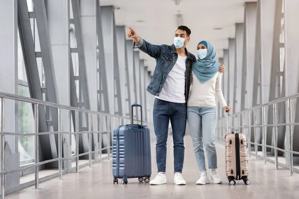 Jóvenes cónyuges islámicos con máscaras médicas protectoras con maletas en el aeropuerto —  Fotos de Stock