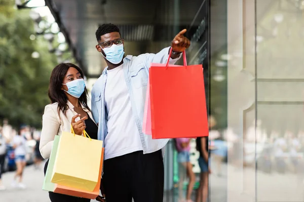 Alışveriş torbalarıyla yürüyen maskeli siyah bir çift.