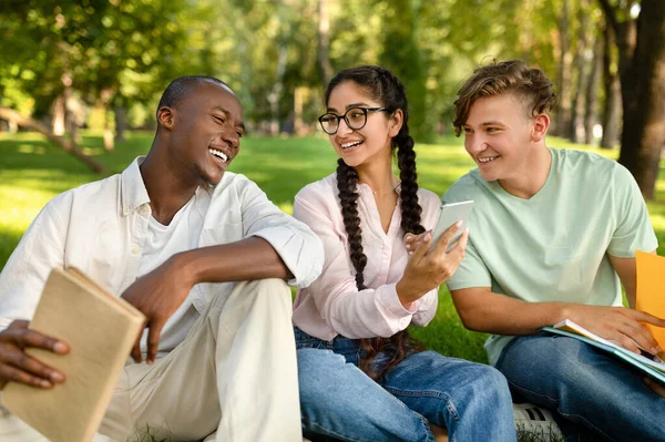 Diverse befreundete Studenten mit Smartphone und neuer Bildungsanwendung sitzen gemeinsam auf dem Campus der Universität — Stockfoto