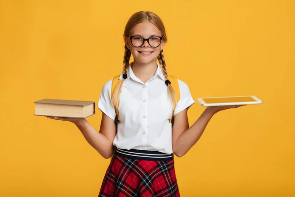 Veselý mladý kavkazský školačka s copánky, batoh v brýlích držet knihu a tablet a vybírá — Stock fotografie