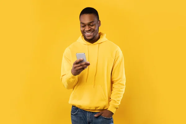노란 배경 위에 서 있는 전화 문자를 사용하는 아프리카 계 미국인 — 스톡 사진
