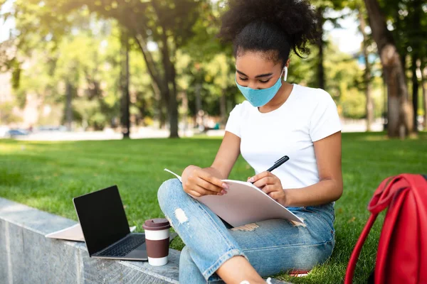 Estudiante negro tomando notas usando máscara facial aprendiendo al aire libre — Foto de Stock