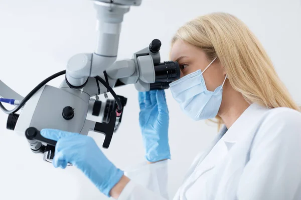 Jovem mulher loira estomatologista olhando para microscópio dentário — Fotografia de Stock