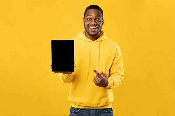 Hombre negro señalando la pantalla vacía de la tableta digital, fondo amarillo —  Fotos de Stock