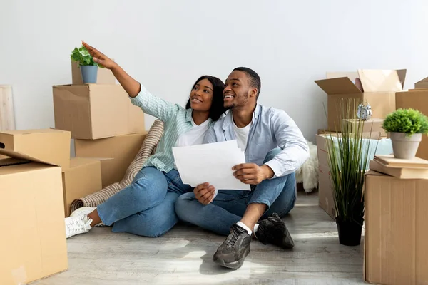 Spannende zwarte echtgenoten zitten met laptop en fantasierijke ontwerp in hun nieuwe flat, bespreken toekomstige interieur — Stockfoto