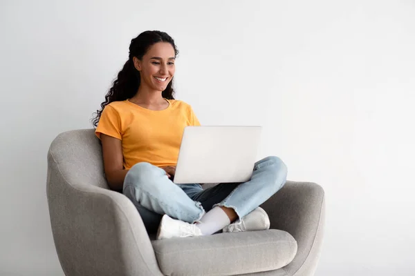 Concepto Independiente. Mujer sentada en sillón con computadora portátil, trabajando remotamente en casa — Foto de Stock