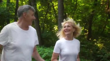 Yeşil halk parkında birlikte koşup sabah koşusundan keyif alan aktif, mutlu kıdemli bir adam ve kadın.