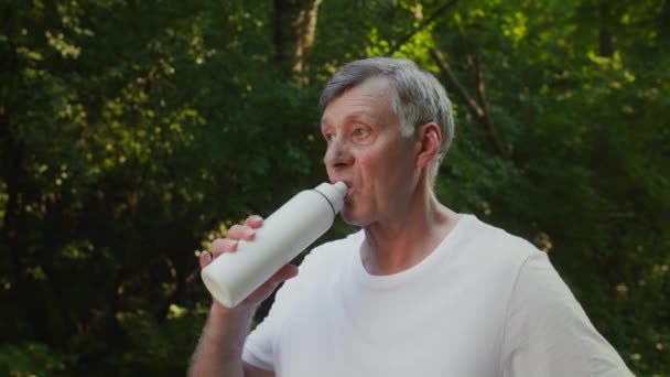 Concepto de deportes e hidratación. Hombre mayor activo bebiendo agua al aire libre, teniendo descanso en la actividad deportiva en el parque público — Vídeo de stock