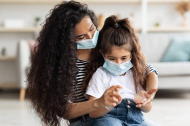 Orta Doğulu anne ve kız dezenfektan kullanarak yüz maskeleri takıyor.